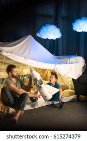 Father And Son Sitting Together In Blanket Fort And Playing With Toy Rocket