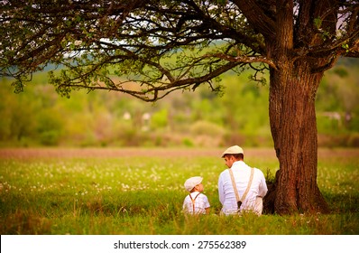 father and son sitting under the tree on spring lawn