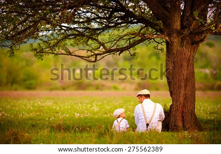 father and son sitting under the tree on spring lawn