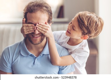 Father And Son Are Smiling While Spending Time Together. Little Boy Is Covering His Dad Eyes