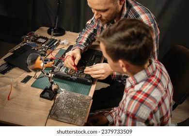 Father and son soldering circuit board or motherboard with soldering iron at home, overhead view. Copy space