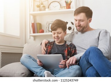 Father and son spending time together and using digital tablet on sofa at home