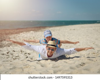 Father and son spending time together on sea beach on summer vacation. Boy is laying on his father back, their arms are open wide. - Powered by Shutterstock