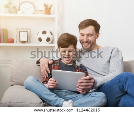 Father and son spending time together and playing on digital tablet on sofa at home