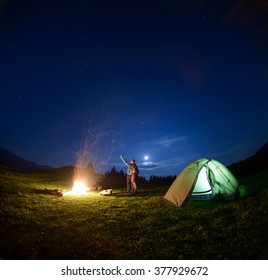 Father and son standing near big campfire and tent looking at beautiful night sky full of stars and enjoying night scene. Man is pointing at the sky - Powered by Shutterstock