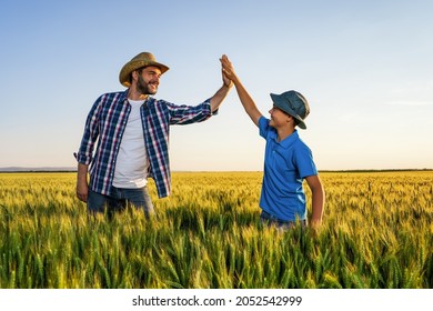 Father and son are standing in their growing wheat field. They are happy because of successful sowing.