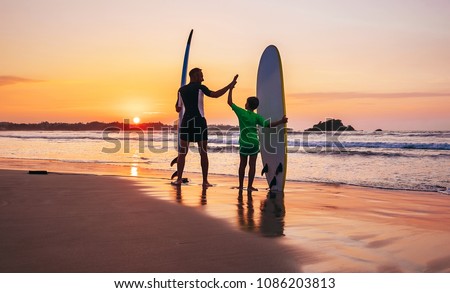 Father and son surfers stay on the sunset beach
