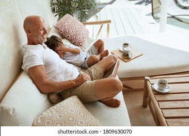 Father And Son With Tablet Resting At Home. Dad With Little Boy Sitting On Sofa, Using Portable Digital Device And Enjoying Family Weekend At Tropical Villa. Summer Vacation With Child As Lifestyle.