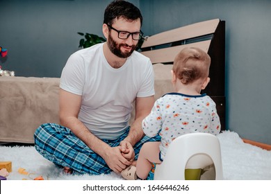 Father And Son. The Father Teaches The Child To Walk On The Potty. The Father Is Very Waiting And Looking At The Baby. Dad Folded His Arms In Anticipation. Baby Toiletries. Potty Training