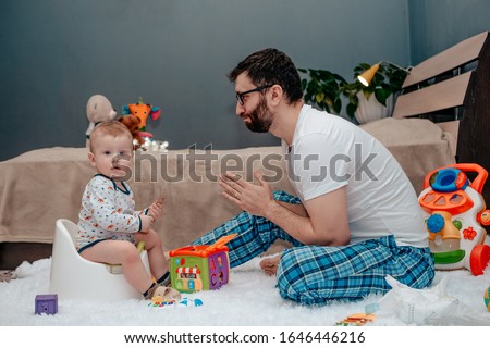Father and son. Father teaches a child to walk on a potty. Father does begs and asks. The child is playing. Baby toiletries. Potty training.