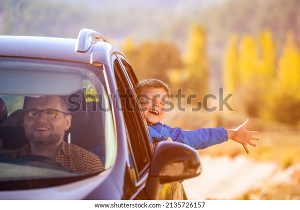 Father with son\
travel by the car. Child boy tourist looking out from auto window\
and greets nature. Driver in the car driving for journey. Family\
travel by car in the\
mountains