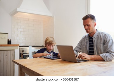 Father and son using computers at the kitchen table