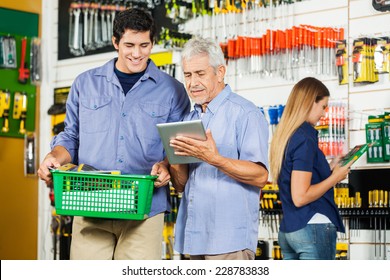 Father And Son Using Digital Tablet In Hardware Store With Female Customer In Background