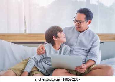 Vater und Sohn benutzen gemeinsam Laptop-Computer auf dem Bett für Technologie-Erziehungskonzept.