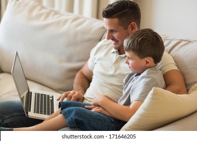 Father and son using laptop while relaxing on sofa at home