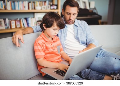 Father and son using laptop while sitting on sofa at home