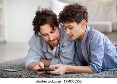 Father and son using smartphone, watching photos or boy helping daddy with game, spending time at home while lying on floor carpet. Modern technologies and leisure activities concept - Powered by Shutterstock
