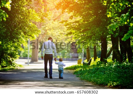 Father and son are walking along the alley in the park holding hands. View from the back. Father's Day.