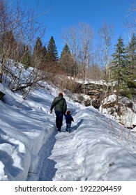 A Father And Son Walking Hand In Hand Along A Snowy Trail In The Wilderness.  They Are Walking Towards A Stair Case Made Of Natural Timber. The Toddler Boy And Man Are Wearing Matching Plaid Hats.