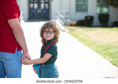 Father and son walking trough school park. Portrait of happy nerd pupil holding teachers hand