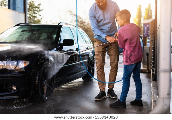 Father and son washing their car at car wash\
station using high pressure\
water.