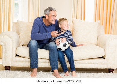 Father And Son Watching Football Match On Tv Sitting On The Sofa