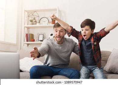 Father and son watching football on TV at home. Emotional man and little boy cheering their favorite team, family enthusiasm, copy space