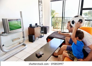 Father And Son Watching Football World Cup Soccer On Tv Together In Living Room On Sofa Being Excited Fans