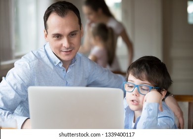 Father and son watching video on computer screen at home. Family leisure time, gadget addiction concept. Smiling husband sitting work on laptop, kid in glasses look at monitor, poor eyesight problem - Powered by Shutterstock