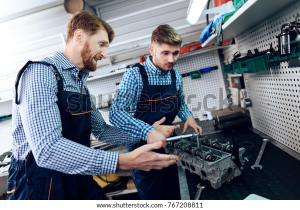 Father and son work at the auto service. Two\
mechanics work with the details of the car. Two auto mechanics are\
arguing about fixing the car\
parts.