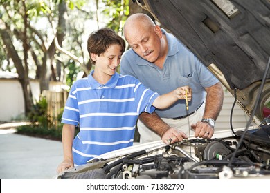 Father and son working on the car together.  The son is checking the oil.