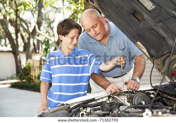 Father and son working on the car together.  The son\
is checking the oil.