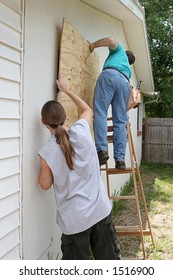A father and son working together to board up their house for a hurricane.