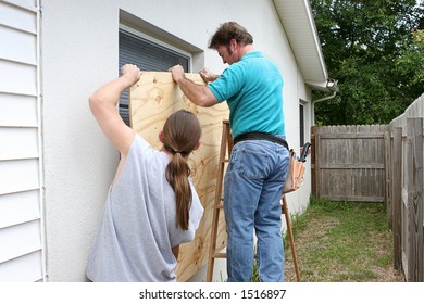 A Father And Son Working Together To Install Plywood Over Windows In Preparation For A Hurricane.