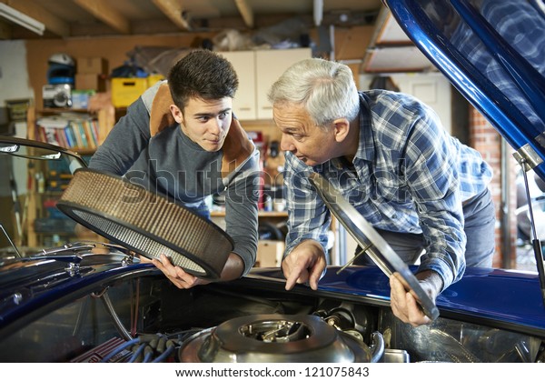 father and son working\
together on a classic car in a garage with air filter cover open\
looking in