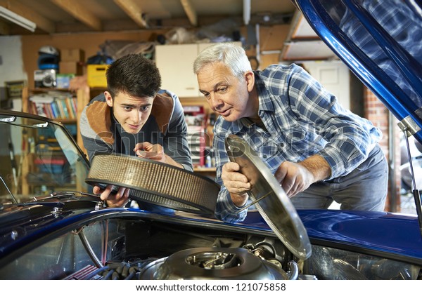 father and son working\
together on a classic car in a garage with air filter cover open\
looking in