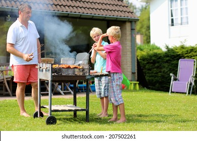 A father with sons, two twin teenage boys cooking meat on barbecue for summer family dinner at the backyard of the house