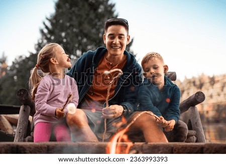 father spending fun time with his children having fun roasting marshmallows over a campfire having fun laughing and playing together  