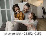 A father is spending quality time with his two daughters, sitting on the floor with them as they draw and color in a book. 