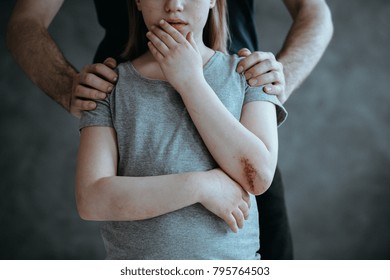 Father standing behind crying young girl with hurt elbow