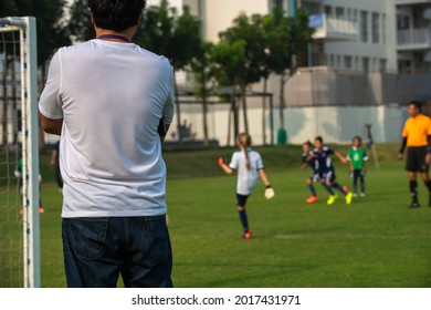 Father Standing And Watching His Daughter Playing Football In A School Tournament On A Sideline With A Sunny Day. Sport, Outdoor Active, Lifestyle, Happy Family And Soccer Mom And Soccer Dad Concepts.