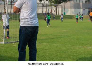 Father Standing And Watching His Daughter Playing Football In A School Tournament On A Sideline With A Sunny Day. Sport, Outdoor Active, Lifestyle, Happy Family And Soccer Mom And Soccer Dad Concepts.