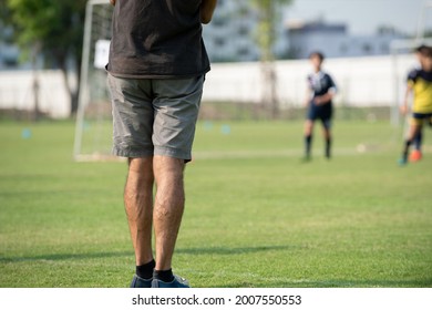 Father Standing And Watching His Son Playing Football In A School Tournament On A Sideline With A Sunny Day. Sport, Outdoor Active, Lifestyle, Happy Family And Soccer Mom And Soccer Dad Concepts.