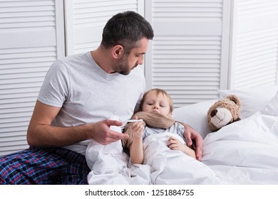 father taking care of sick son in bedroom and checking his temperature with thermometer - Powered by Shutterstock