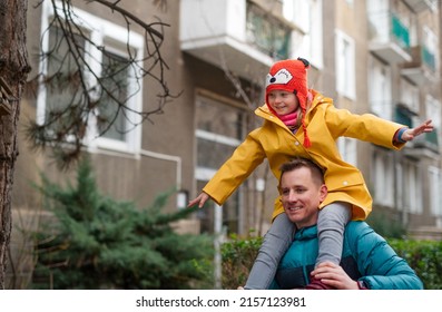 Father taking his little daughter with Down syndrome on piggyback to school, outdoors in street.