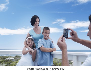 Father Taking A Portrait Photo Of Happy Family At Vacation Beach House Balcony