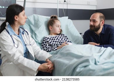 Father Talking To Pediatrist Expert About Recovery Therapy While In Healthcare Pediatric Hospital Patient Ward Room. Pediatric Clinic Doctor Specialist Conversating With Man About Daughter Condition.