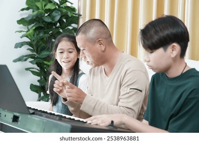 A father teaches his eight-year-old daughter to play musical instruments and his fourteen-year-old friend, a boy, practices playing the keyboard or the electric tone and plays music together at home. - Powered by Shutterstock