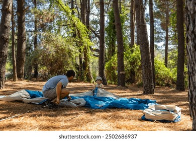 A father teaches his son to pitch his tent in the forest. Camping - Powered by Shutterstock