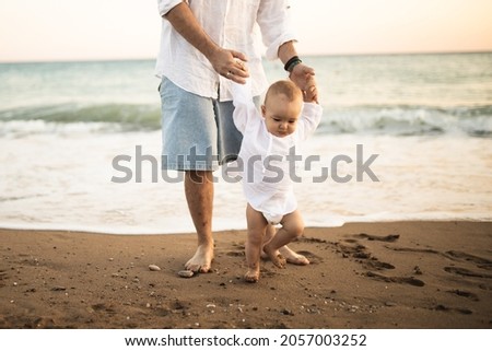 A father teaches his son to walk. The first steps of the child. The pastime of dad and son. Happy fatherhood. Dad and his little son near the sea. Rest at the sea.